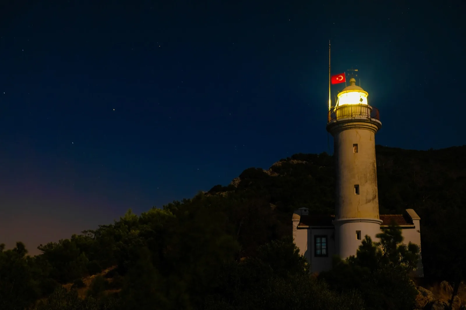 Gece gökyüzü altında ışığı yanan Gelidonya Feneri ve çevresindeki kayalık arazi