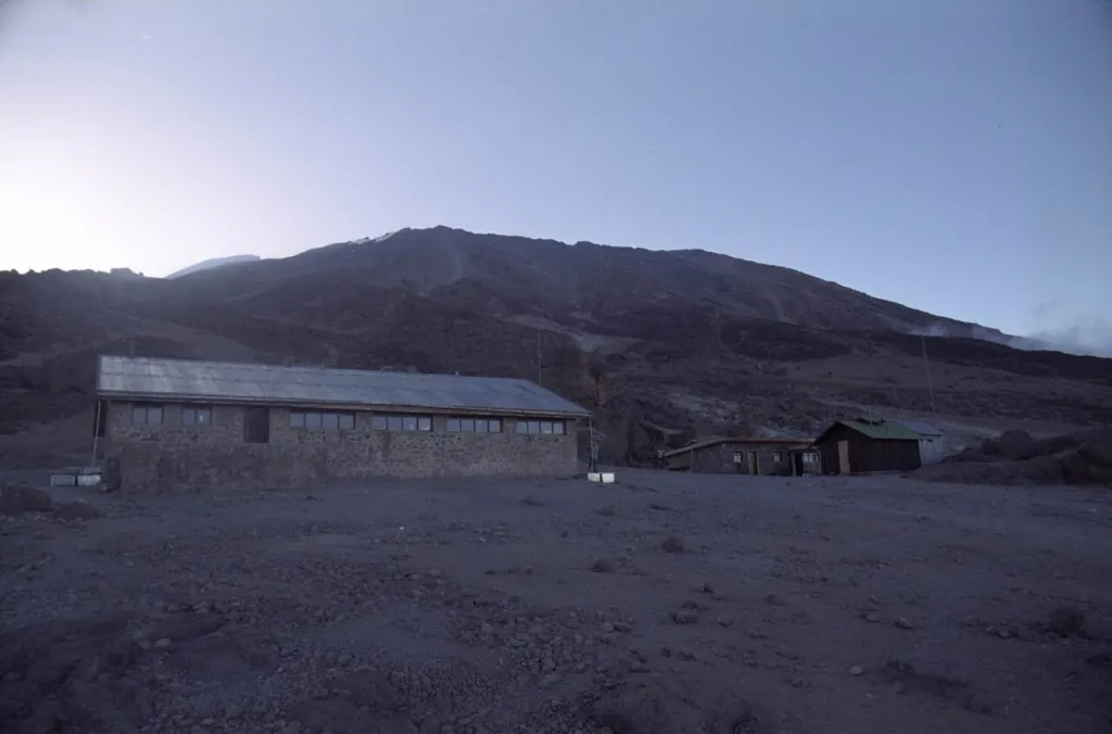 Kilimanjaro'da Marangu rotasının son konaklama noktası Kibo Hut'ın taş binası; arkada şafak ışığında Kibo zirvesinin yamacı