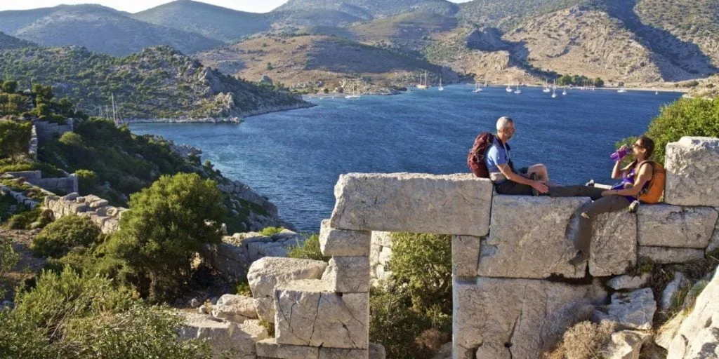 Karia Yolu antik taş kalıntılarında deniz manzarasına karşı mola veren yürüyüşçüler